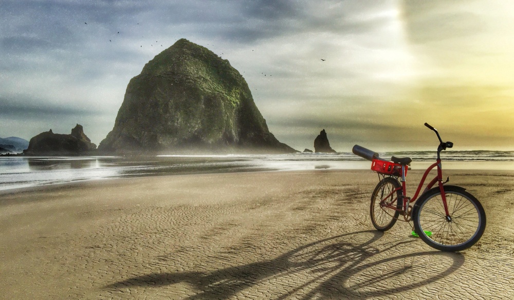 Haystack Rock with the shadow from a red bicycle on the shoreline of Cannon Beach, Oregon.