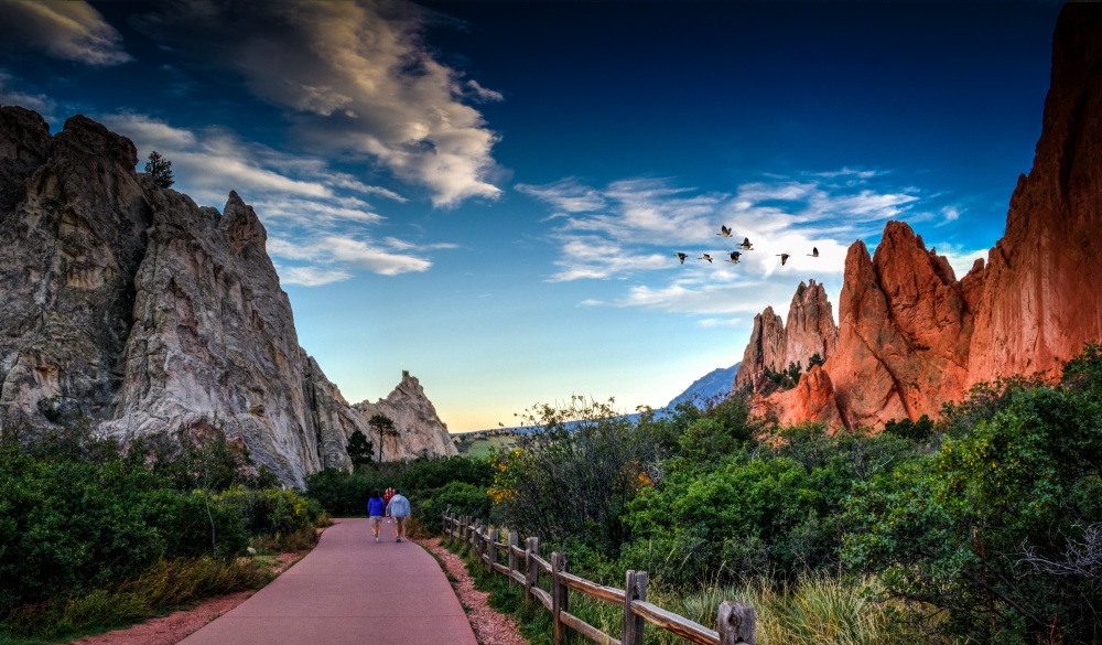 People Walking On Footpath By Rock Formation And Plants Against Sky At Colorado Springs